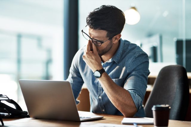Frustrated man pinching nose under his glasses